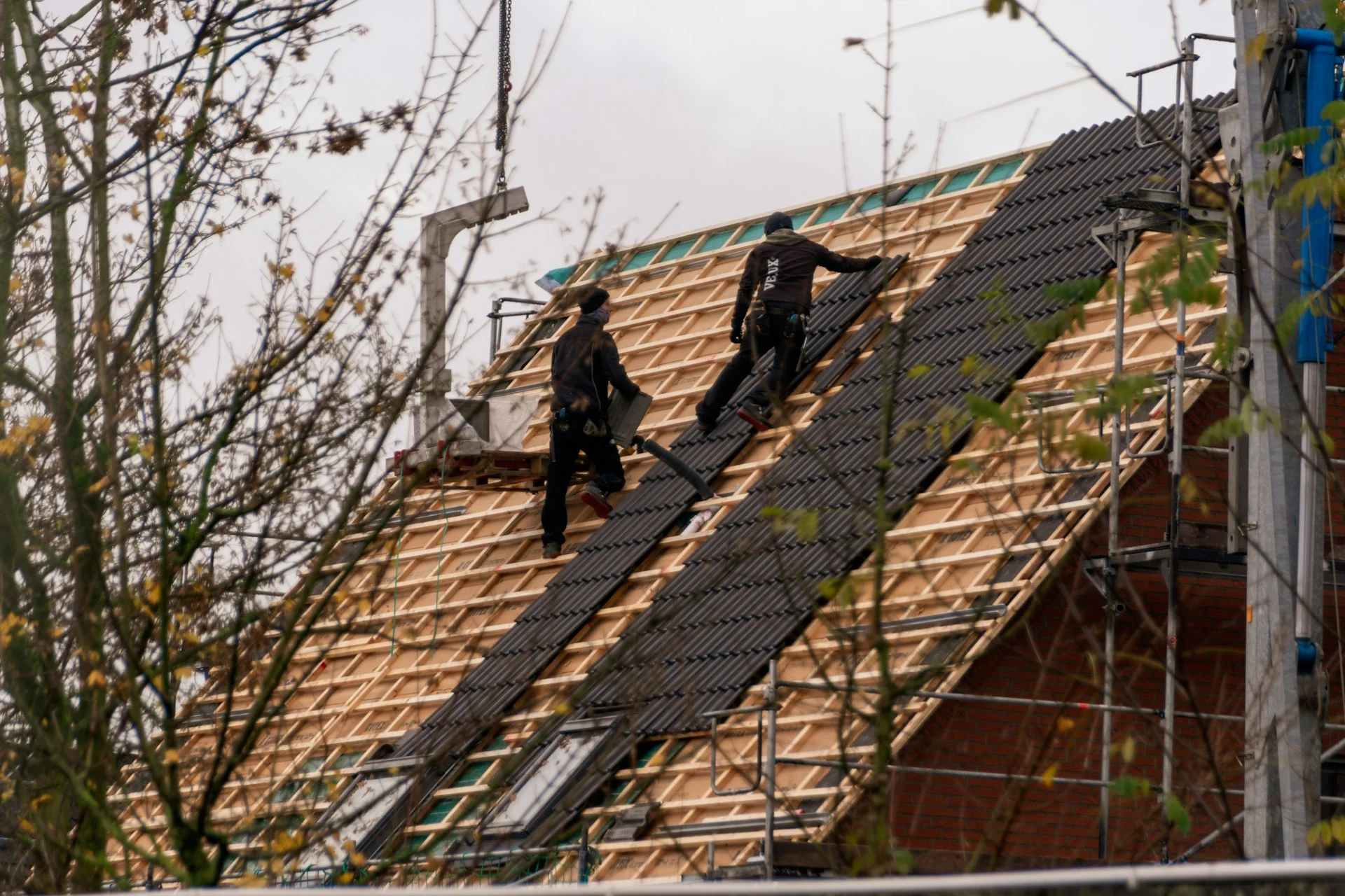 Two roofing workers installing tiles on a pitched roof